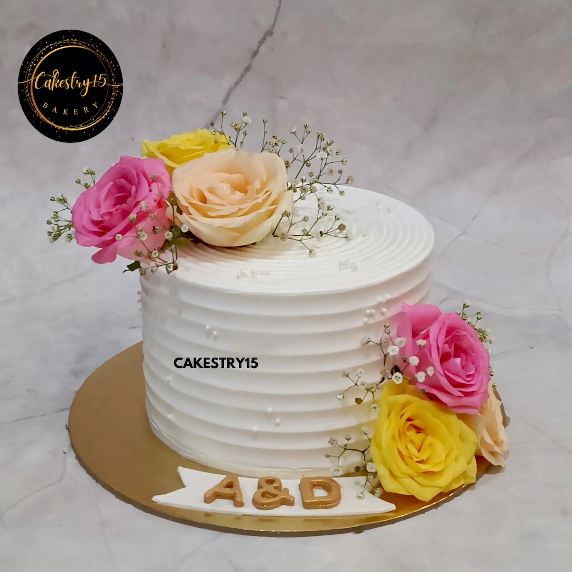1kg eggless butterscotch cake with pink, yellow, and ivory roses, A&D initials on base