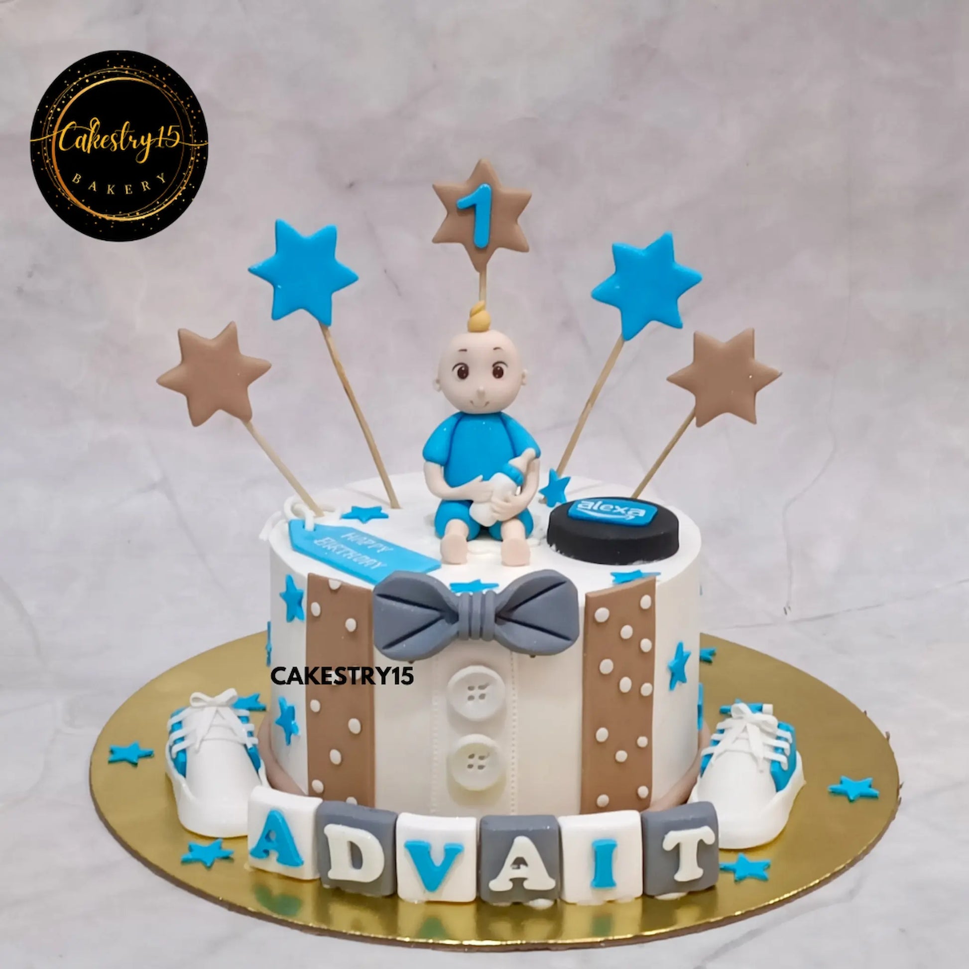 Advait’s 1st birthday cake in choco butterscotch with baby figurine, bowtie, fondant name blocks, and white shoes from Cakestry15