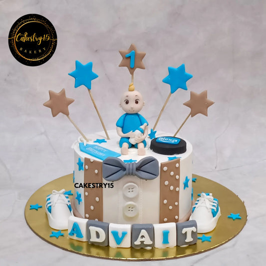 Advait’s 1st birthday cake in choco butterscotch with baby figurine, bowtie, fondant name blocks, and white shoes from Cakestry15