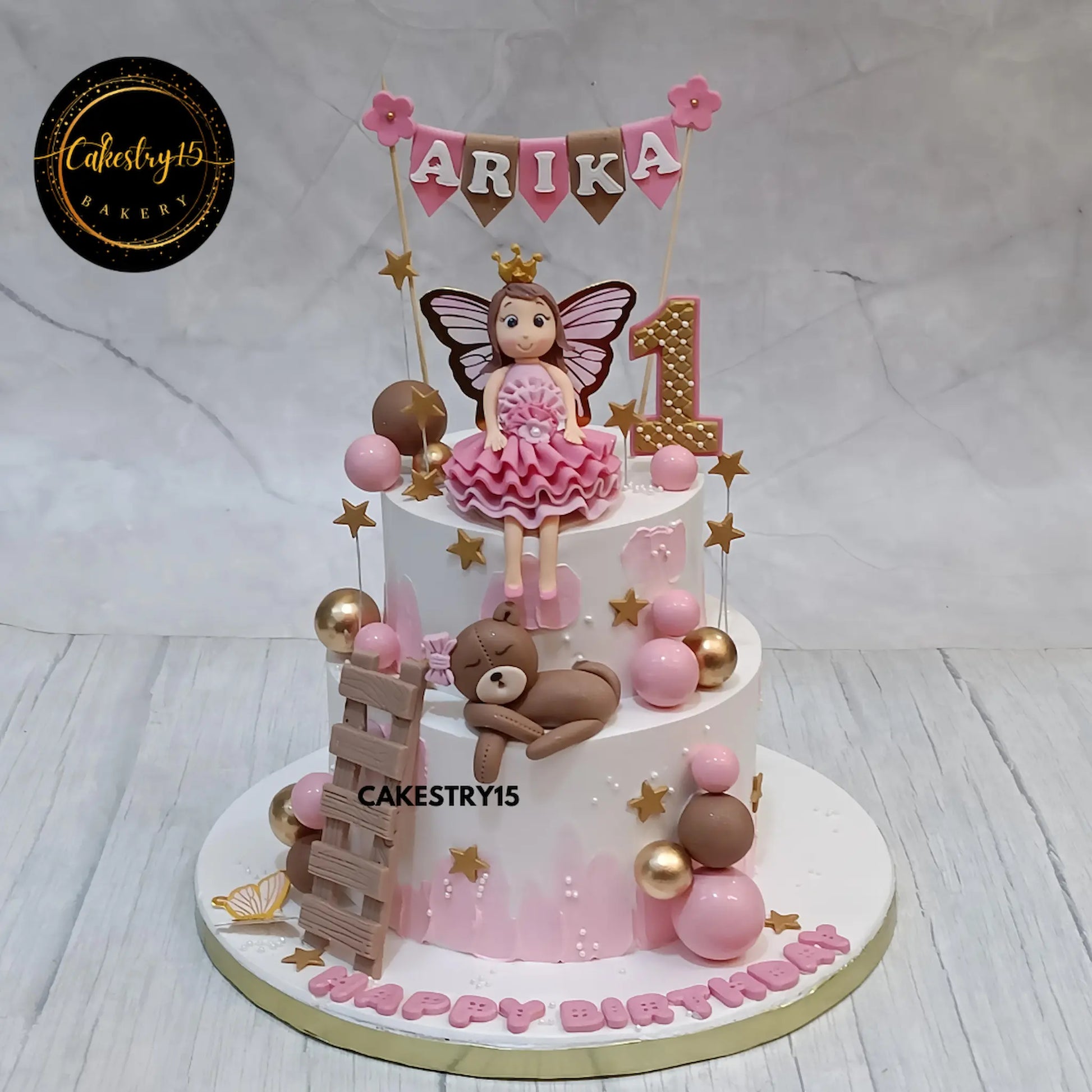 2kg chocolate two-tier cake for Arika's first birthday with girl topper, teddy, and pink-brown accents