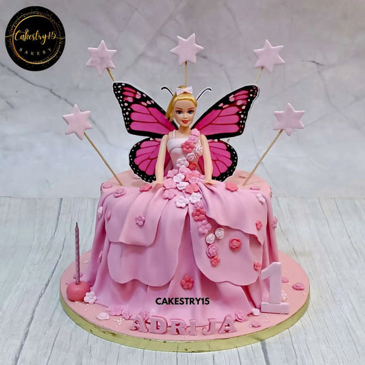 Barbie-themed birthday cake with a real Barbie doll in a pink fondant gown, decorated with fondant stars and paper wings by cakestry15 noida