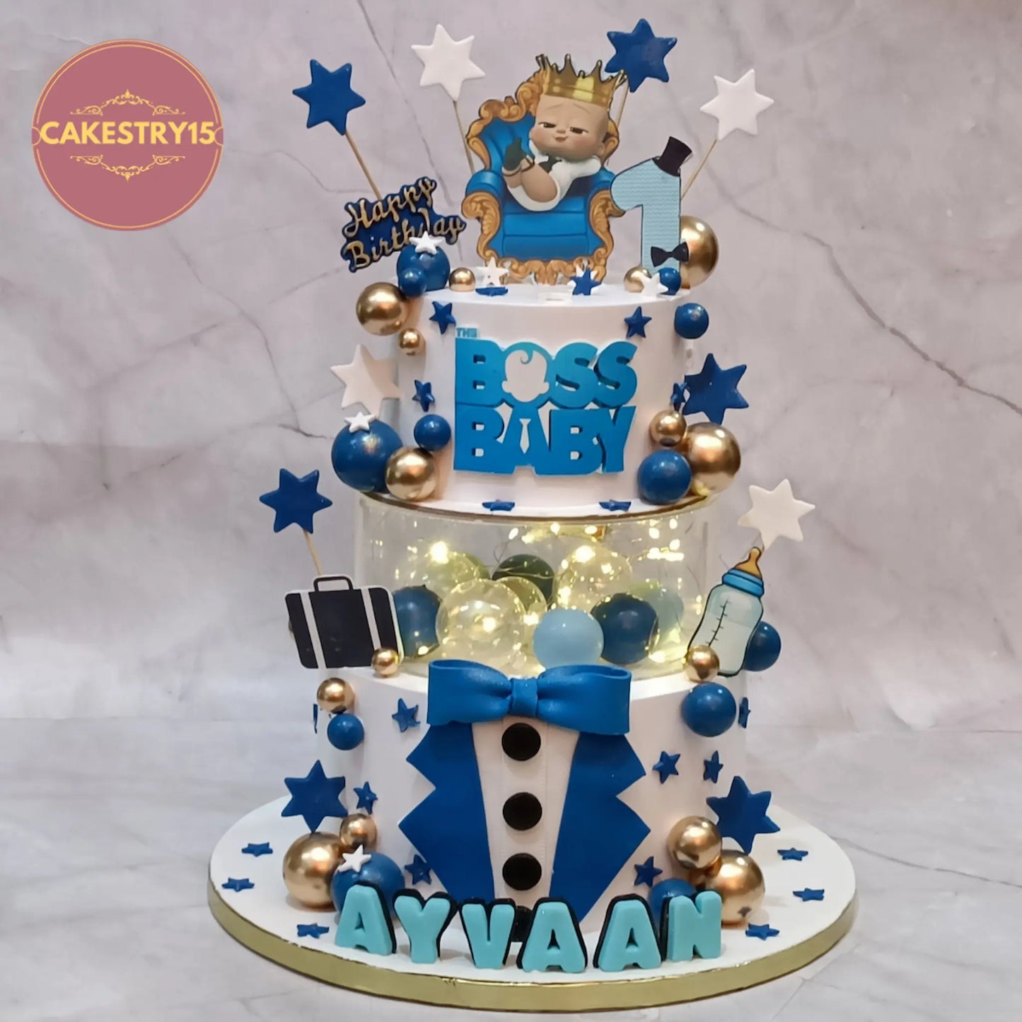 Boss Baby theme first birthday cake with tuxedo design, spacer with lights, logo, and edible elements in eggless choco vanilla by Cakestry15 Noida