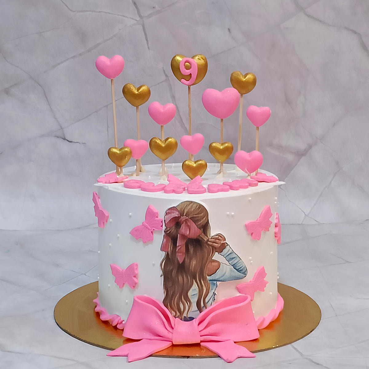 Butterfly theme birthday cake for girls decorated with pink and golden hearts, an edible girl image with a pink bow, and fondant pink butterflies.