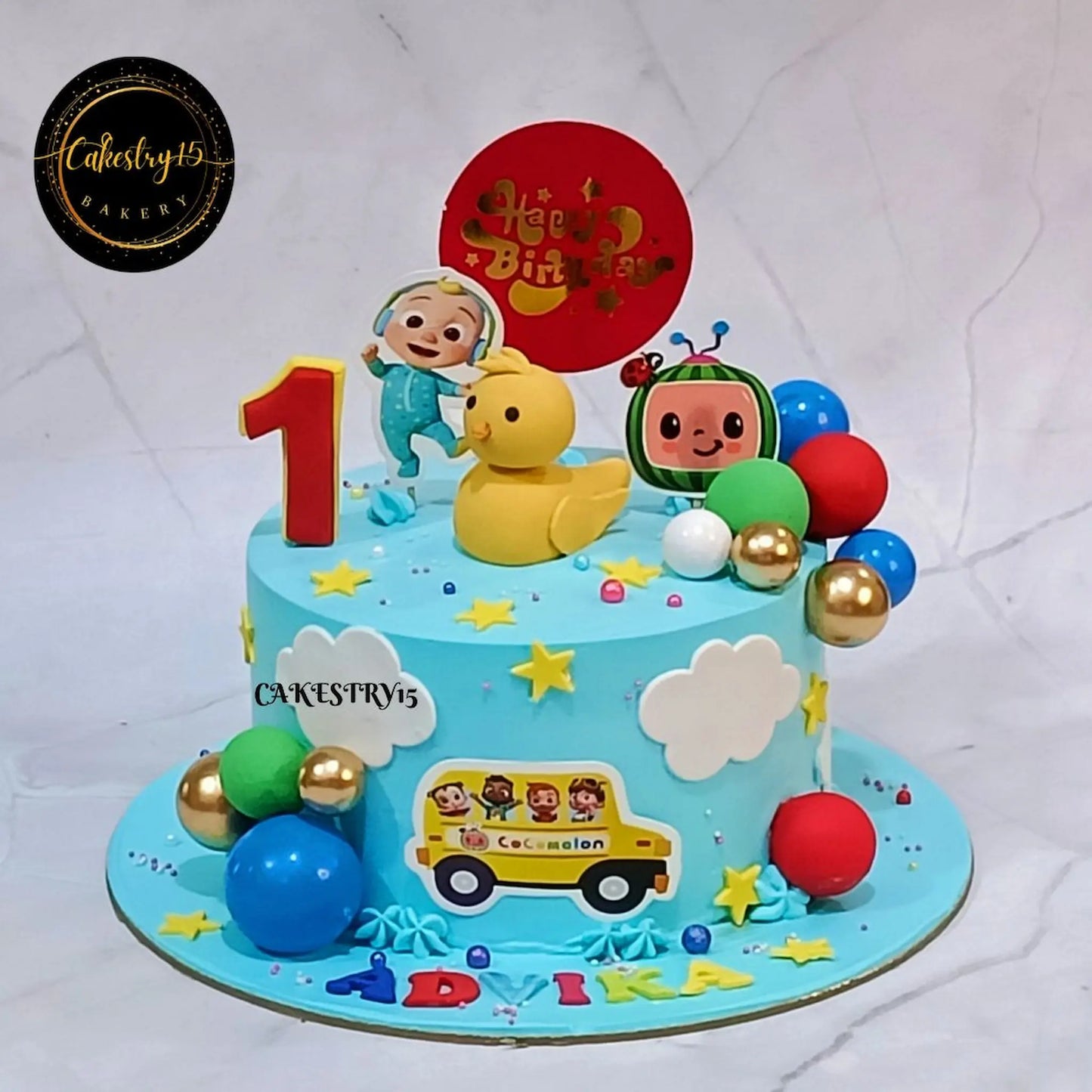 Cocomelon happy first birthday cake for kids with blueberry flavour, eggless theme cake in Noida with colorful toppers and custom name design
