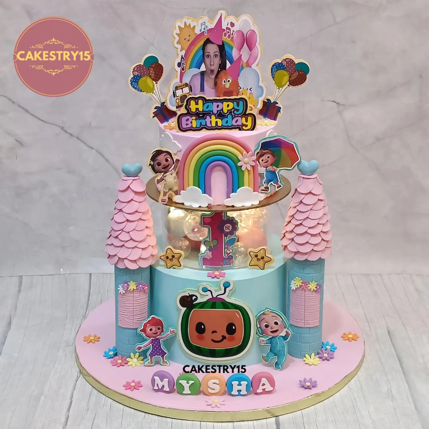 3kg pineapple Cocomelon and Ms Rachel first birthday cake with pillars, rainbow, lights, and edible toppers from Cakestry15 Noida.