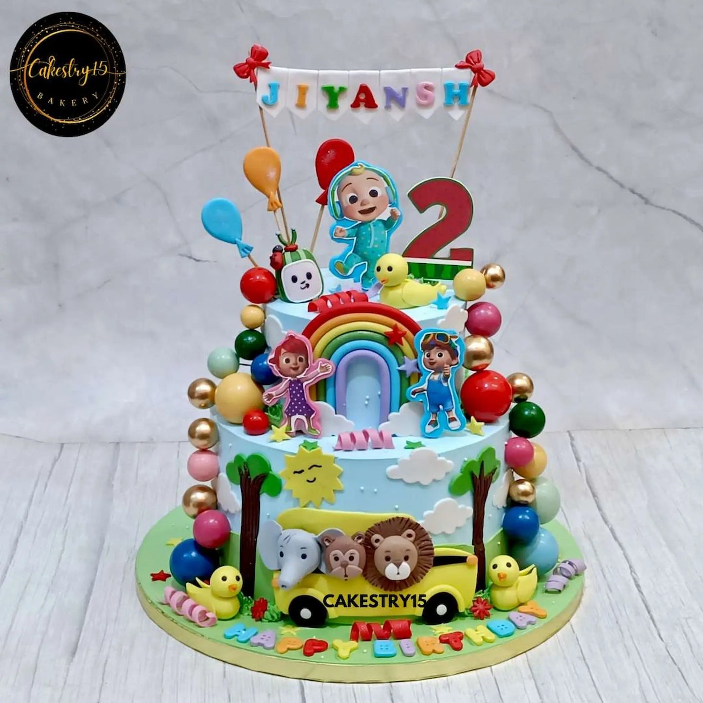 Cocomelon-themed 2-tier birthday cake with edible characters, fondant bus, balloons, and colorful decorations by cakestry15,best bakery noida