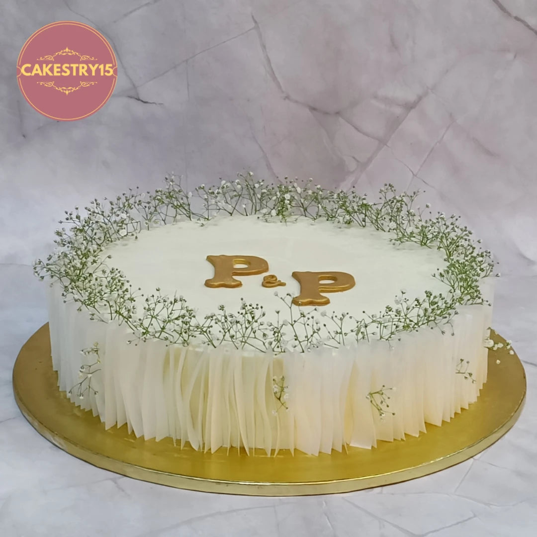 Elegant engagement theme cake Noida featuring baby's breath, rice paper cutouts and white ganache. Premium eggless cake handcrafted for engagement celebrations.