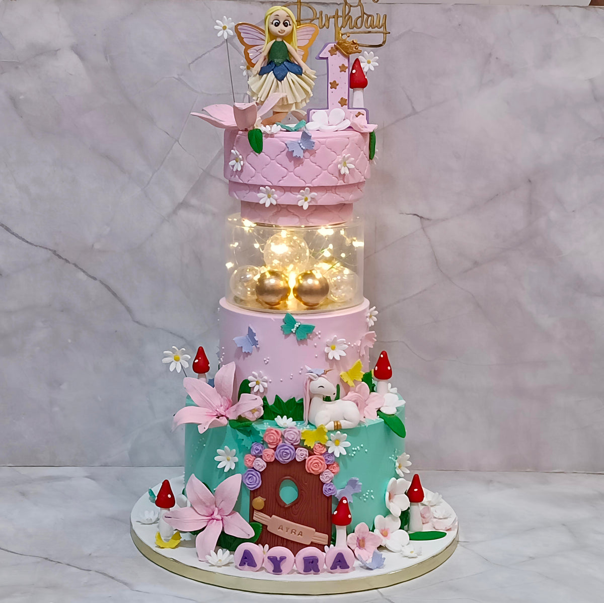 Fairy theme kids birthday cake with a castle door, unicorn detailing, fondant flowers and a fairy figurine, designed as an eggless theme cake in Noida.