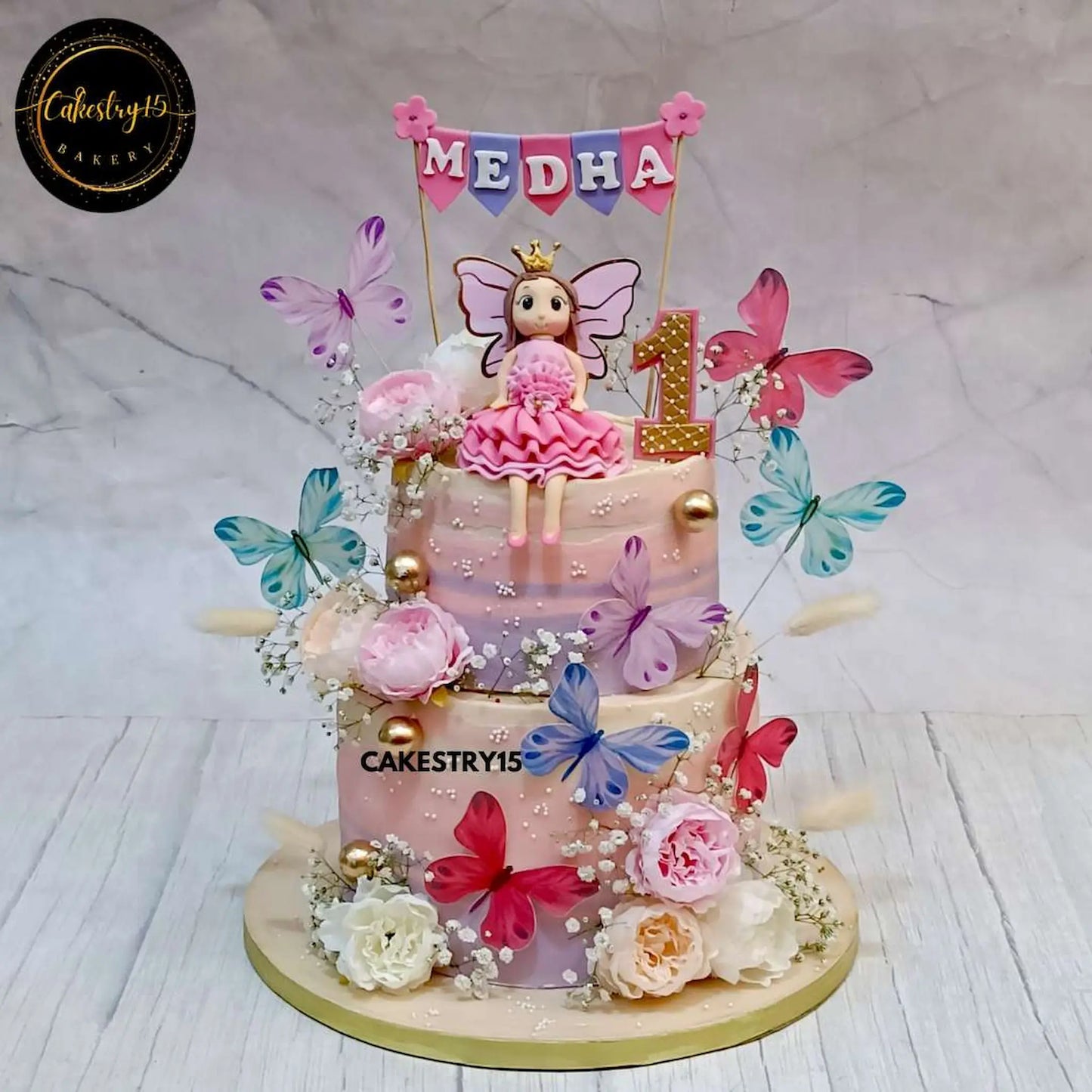 A beautifully designed 3kg, two-tiered choco vanilla doll-themed birthday cake with lavender and ivory shades, a fondant girl figurine, faux flowers, and paper butterflies by cakestry5,best bakery noida