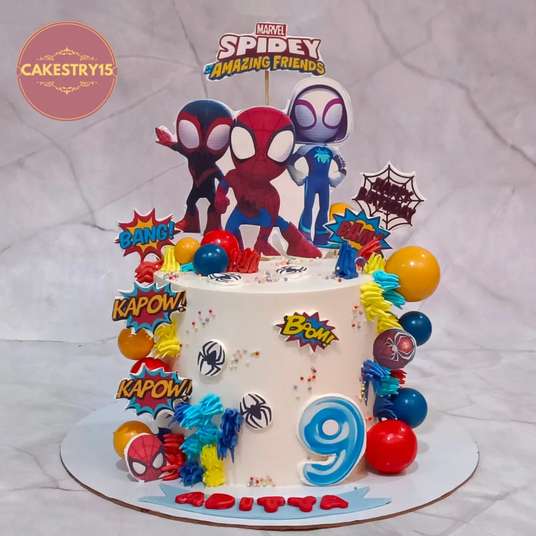A decorated white birthday cake with Spider-Man and Marvel-themed toppers, including Spider-Man, Spider-Gwen, comic book speech bubbles, colorful balloons, and a blue number 9, shown on a marble-patterned background.