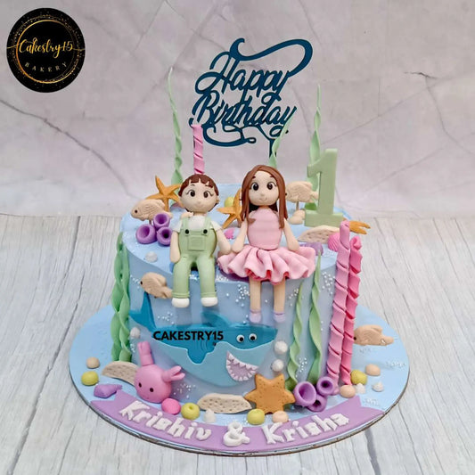 A 2kg chocolate-vanilla under-the-sea-themed birthday cake for twins, featuring boy and girl figurines, coral, fish, crab, shark, starfish, and an Age 1 tag by cakestry15 noida, best bakery noida