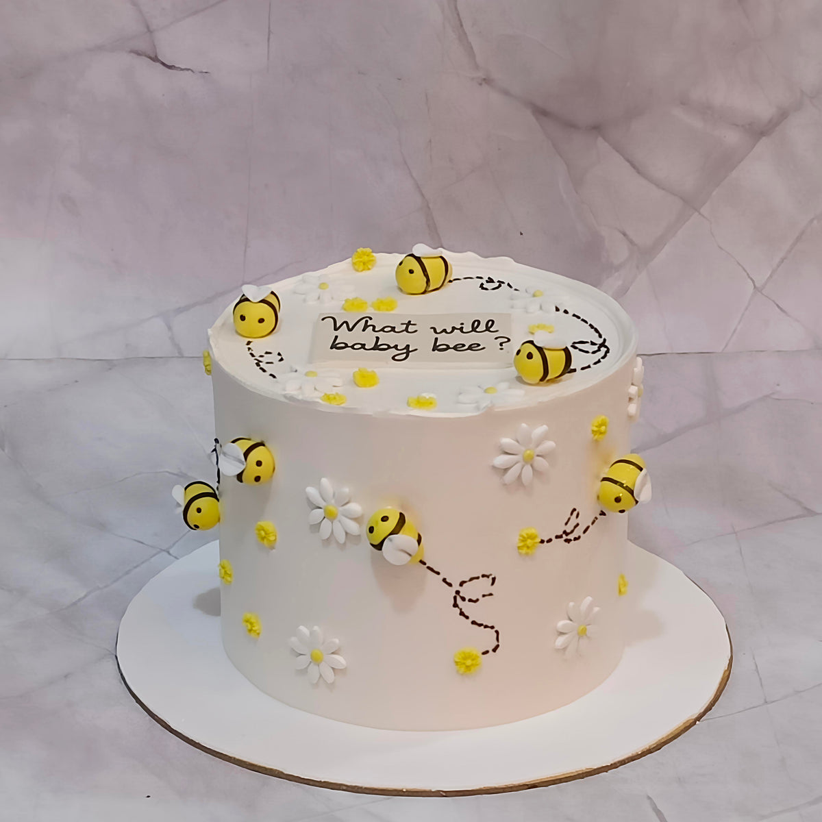 Welcome baby bee theme cake decorated with little fondant bees, white flowers and a “What Will Baby Bee?” tag on top.