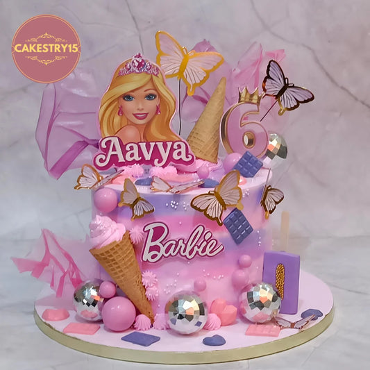 A pink and purple Barbie-themed birthday cake with a Barbie topper, butterfly decorations, ice cream cone props, silver disco ball ornaments, and a large number 6 topper, displayed on a light marble background.