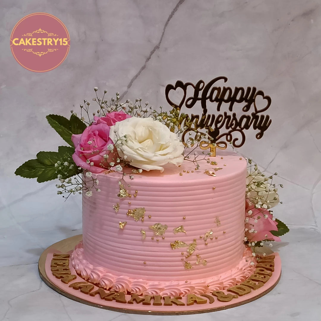 Premium eggless strawberry anniversary cake with fresh roses, baby's breath and golden foil, handcrafted for elegant celebrations in Noida.