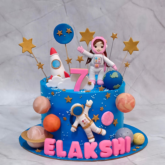 Astronauts and planets space theme cake with blue icing, two fondant astronaut figurines, a rocket and golden stars.