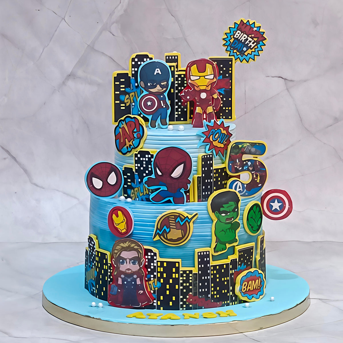A custom two-tiered superhero-themed birthday cake decorated with Marvel characters including Captain America, Iron Man, Spider-Man, Hulk, Thor, and a large number 5, set against a light gray marble-patterned backdrop.