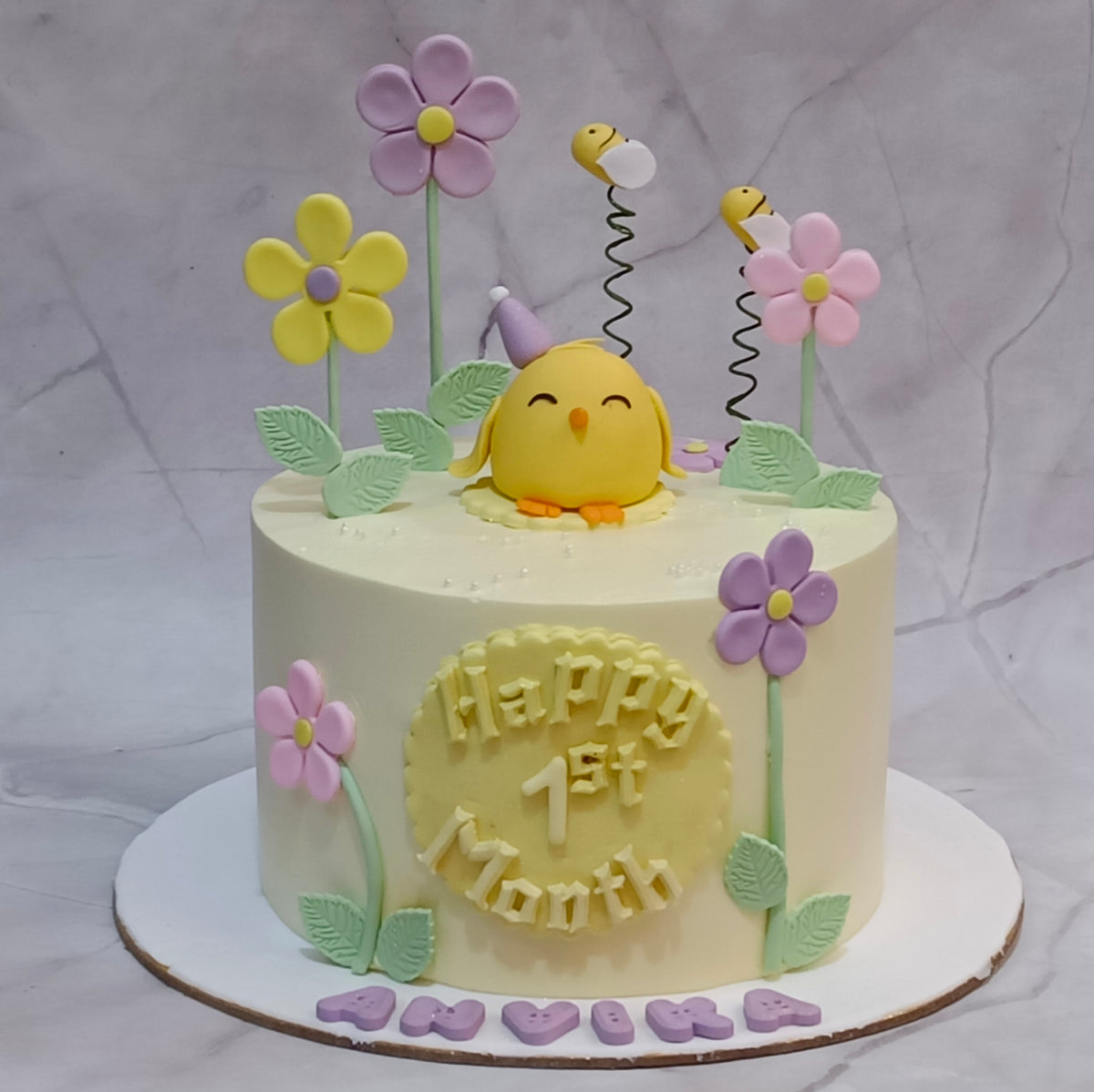 Bees and flowers kids birthday cake with a chick, leaves and a first-month message, from an eggless cakes bakery offering a theme cake in Noida.