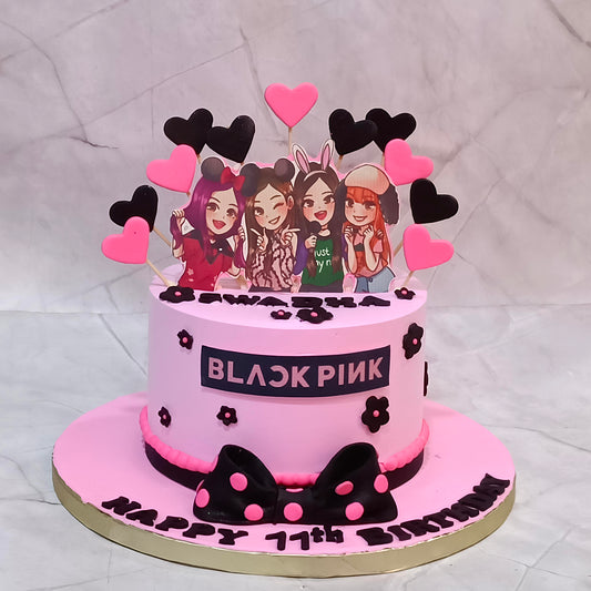 Blackpink birthday cake with edible pop group images, black and pink hearts, and a decorative bow at the base.