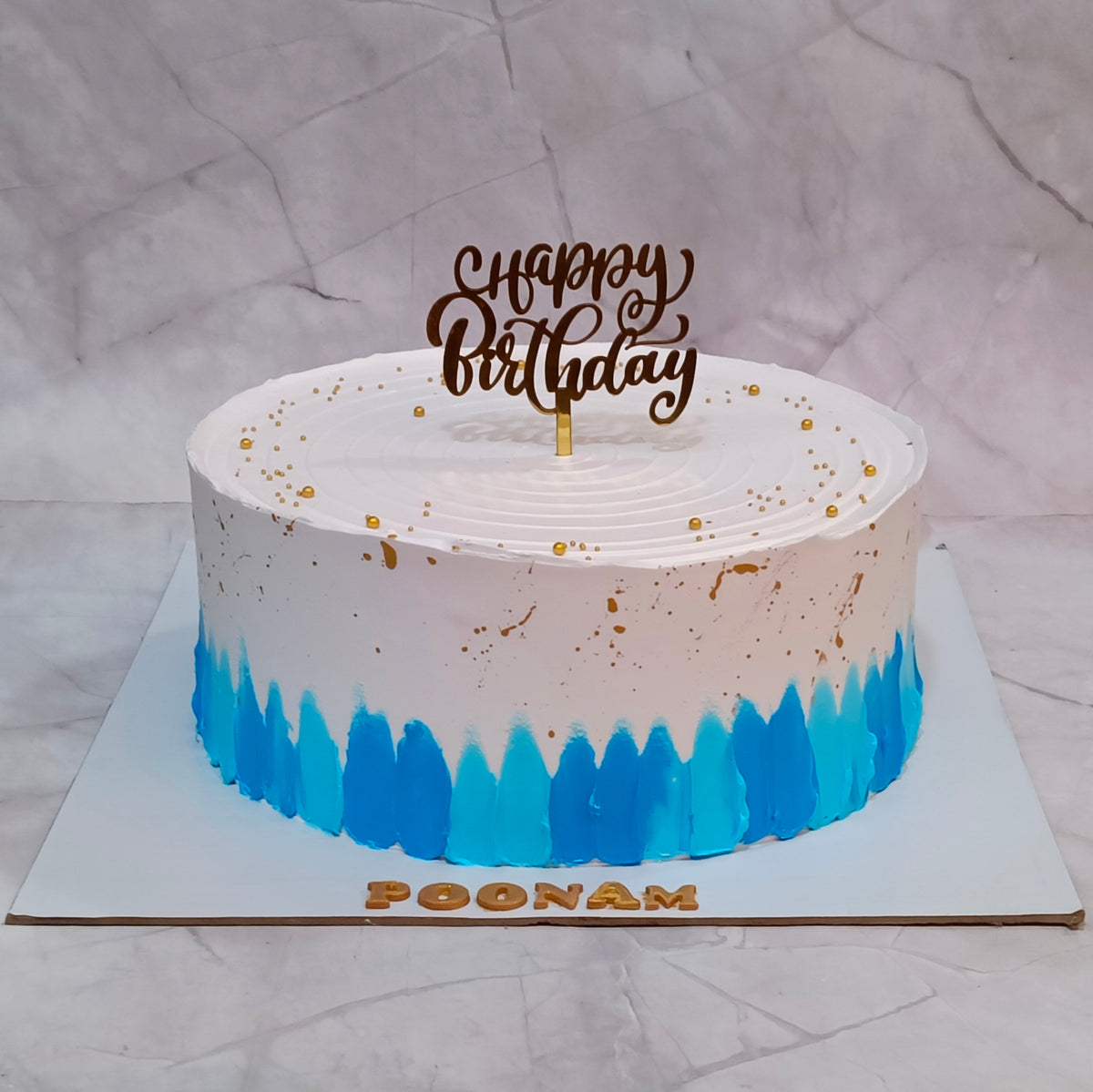 Blue and gold kids birthday cake with white frosting, gold speckles and blue drip decoration, featuring a personalised topper, from our eggless cakes collection and available as a theme cake in Noida.