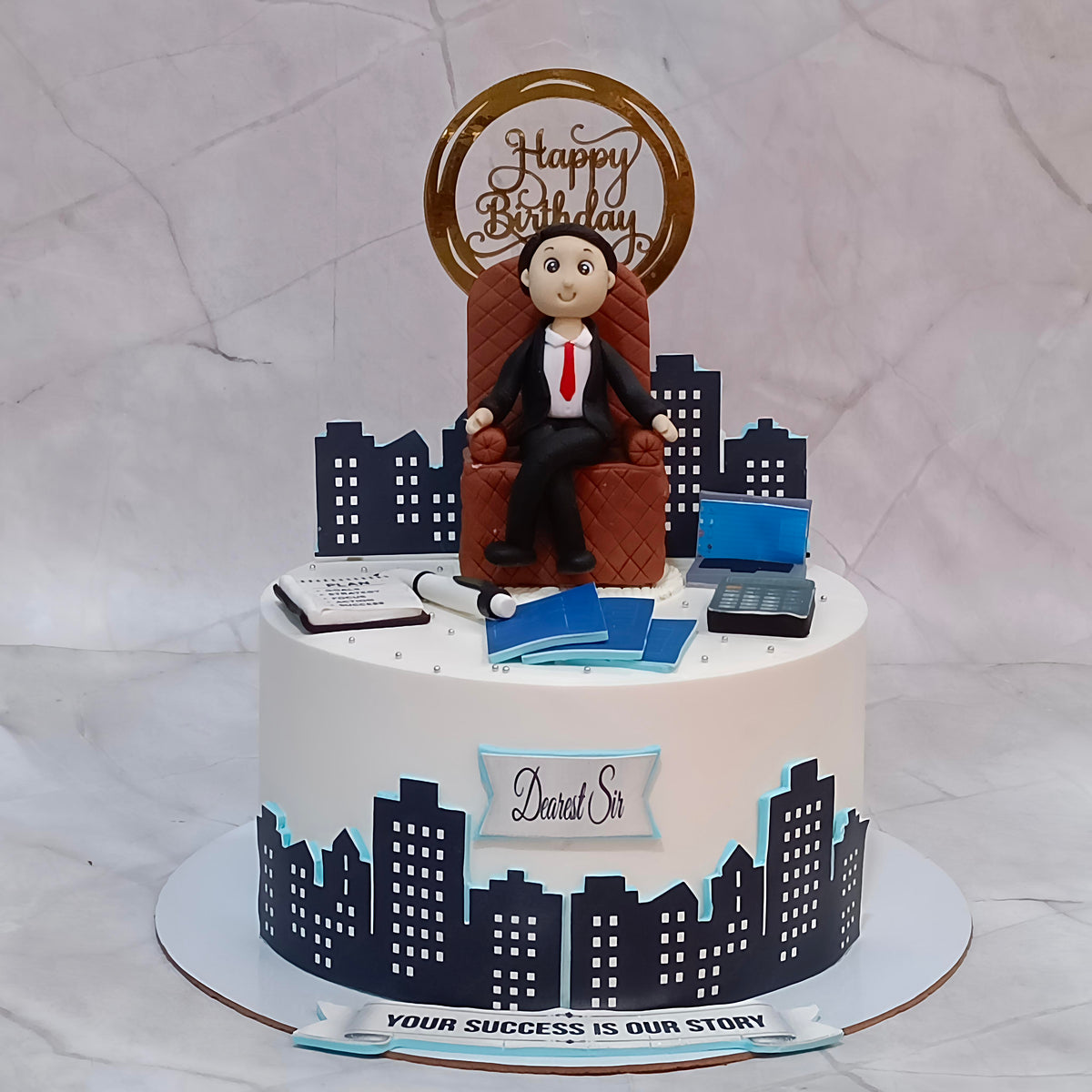 Boss birthday cake in chocolate truffle flavour with a seated man surrounded by edible images of buildings, files, folders, a calculator and a laptop.