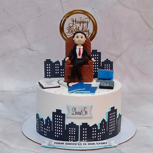 Boss birthday cake in chocolate truffle flavour with a seated man surrounded by edible images of buildings, files, folders, a calculator and a laptop.