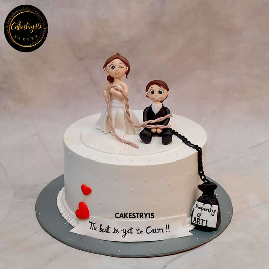 A fun and bold 2kg Black Forest bachelorette cake featuring a bride holding a groom tied up with chains and a bag that says “Property of Arti by cakestry15,best bakery noida