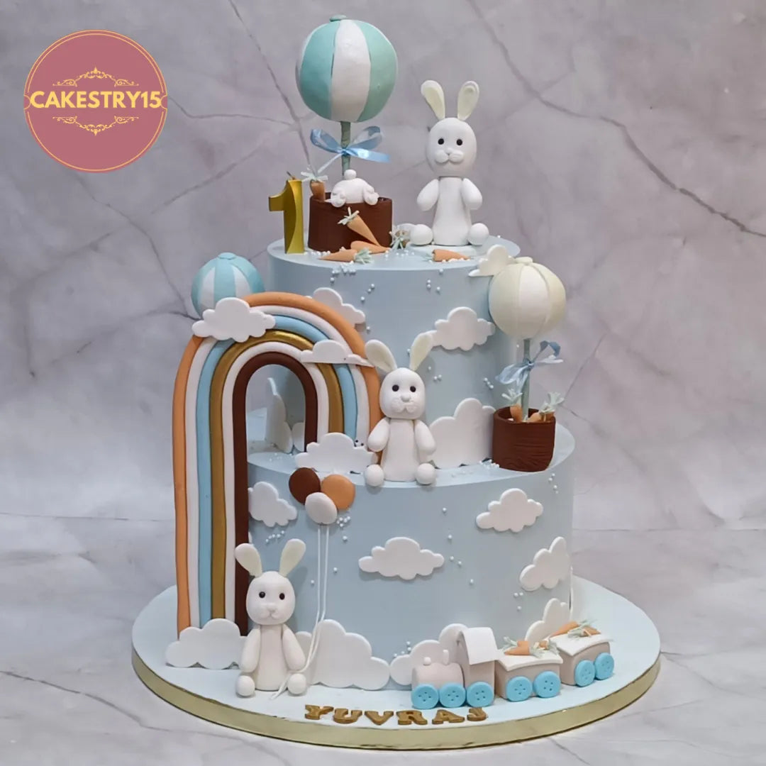 Eggless bunny theme kids birthday cake in Noida with fondant bunnies, rainbow and balloons for a first birthday celebration.