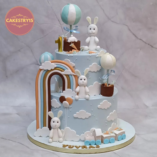 Eggless bunny theme kids birthday cake in Noida with fondant bunnies, rainbow and balloons for a first birthday celebration.