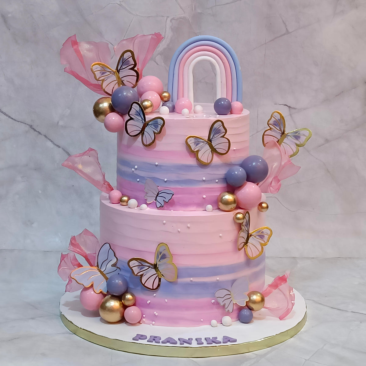 A butterfly rainbow theme kids birthday cake with faux butterflies, fondant rainbow and sugar sails from an eggless cakes bakery offering a theme cake in Noida.