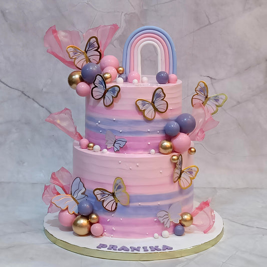 A butterfly rainbow theme kids birthday cake with faux butterflies, fondant rainbow and sugar sails from an eggless cakes bakery offering a theme cake in Noida.