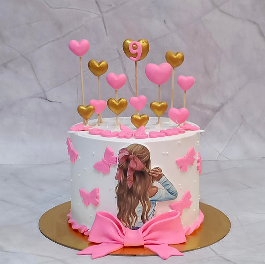 Butterfly theme birthday cake for girls decorated with pink and golden hearts, an edible girl image with a pink bow, and fondant pink butterflies.