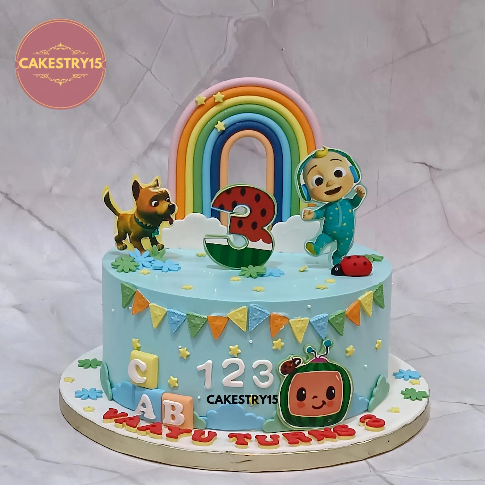 Cocomelon cartoon theme kids birthday cake eggless pineapple cake in Noida with rainbow topper and edible characters for Vaayu birthday celebration