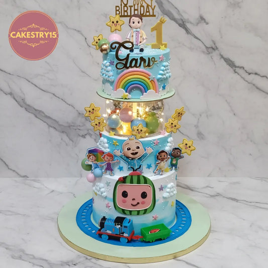 A custom three-tiered birthday cake decorated with JoJo's Bizarre Adventure characters, including Bobo Chose, a rainbow, clouds, and Thomas the Tank Engine, displayed on a marble surface.