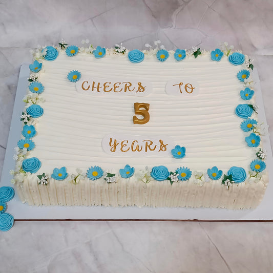 Rectangular corporate 5th anniversary cake with blue fondant roses, faux baby’s breath and “Cheers to 5 Years” written in the centre.