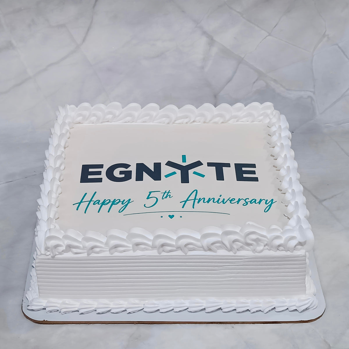 Square Egnyte 5th anniversary corporate photo cake with white icing, piped borders and an edible image in the centre.