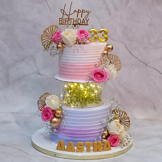 Floral birthday cake with fresh roses, baby’s breath, gecko leaves, faux balls and an illuminated spacer between the tiers.