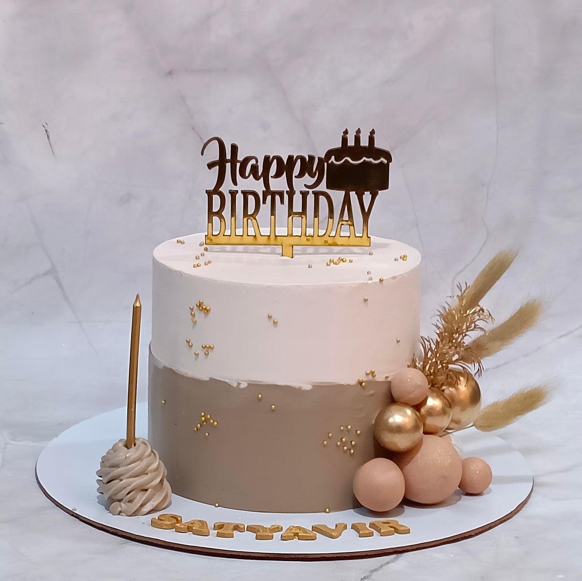 Floral fern butterscotch birthday cake with ivory and dark brown icing, faux balls, a birthday tag and candle.