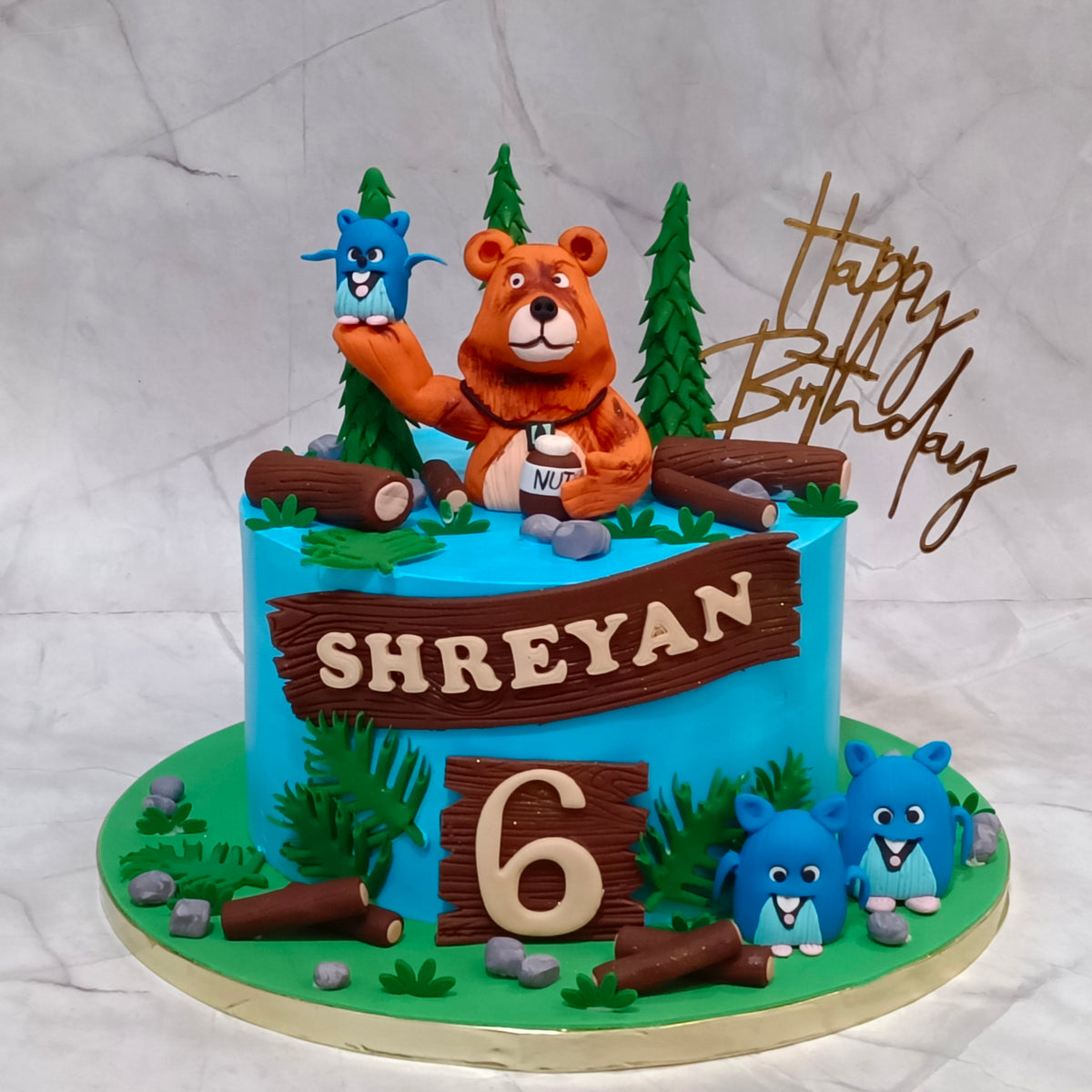 Grizzy and the Lemmings theme cake featuring bear and lemmings figurines, trees, wood logs and leaves for a kids birthday cake in Noida, made as an eggless cake.