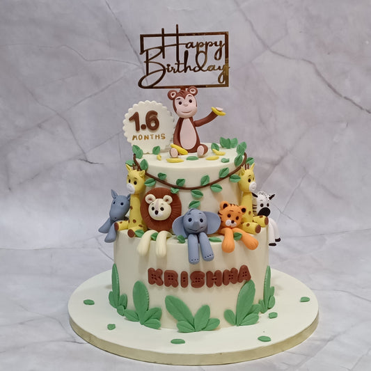 A decorated two-tier jungle birthday cake with jungle animal figures, green leaf accents, a 'Happy Birthday' topper, and a '1.6 months' plaque