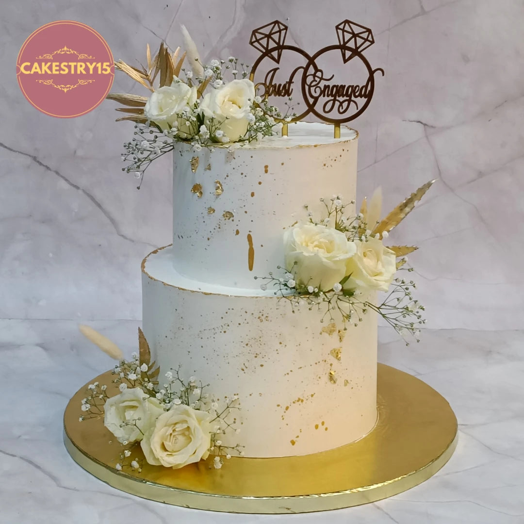 Elegant floral theme cake Noida featuring fresh white roses, baby breath and golden accents, handcrafted as premium eggless cakes for engagement celebrations.