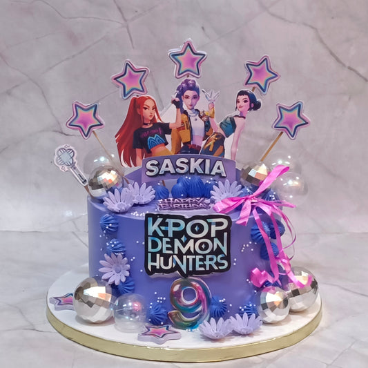A custom purple birthday cake for a K-pop fan named Saskia, decorated with 'K-POP DEMON HUNTERS' text, character cutouts, star toppers, and silver disco ball accents, set on a marble-patterned background.