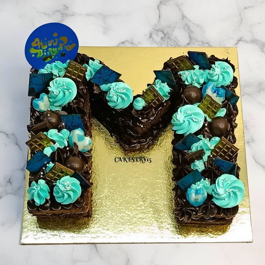 A kids birthday cake in M shape with dark chocolates and cream rosettes, available as a theme cake Noida from an eggless cakes bakery.