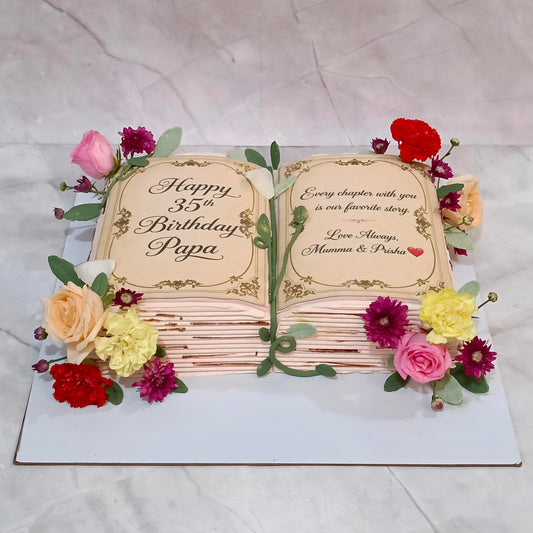 A decorative cake shaped like an open book, with the left page reading 'Happy 35th Birthday Papa' and the right page reading 'Every chapter with you is our favorite story. Love Always, Mama 