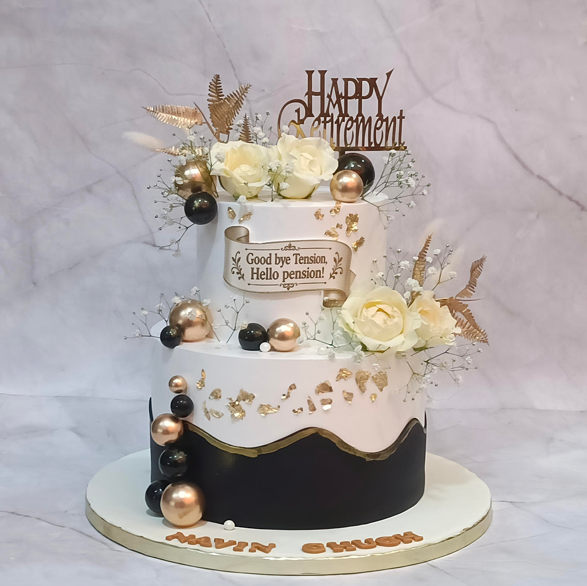 Two-tier retirement floral celebration cake with fresh roses, baby’s breath, faux ferns, golden foil and a Happy Retirement tag.