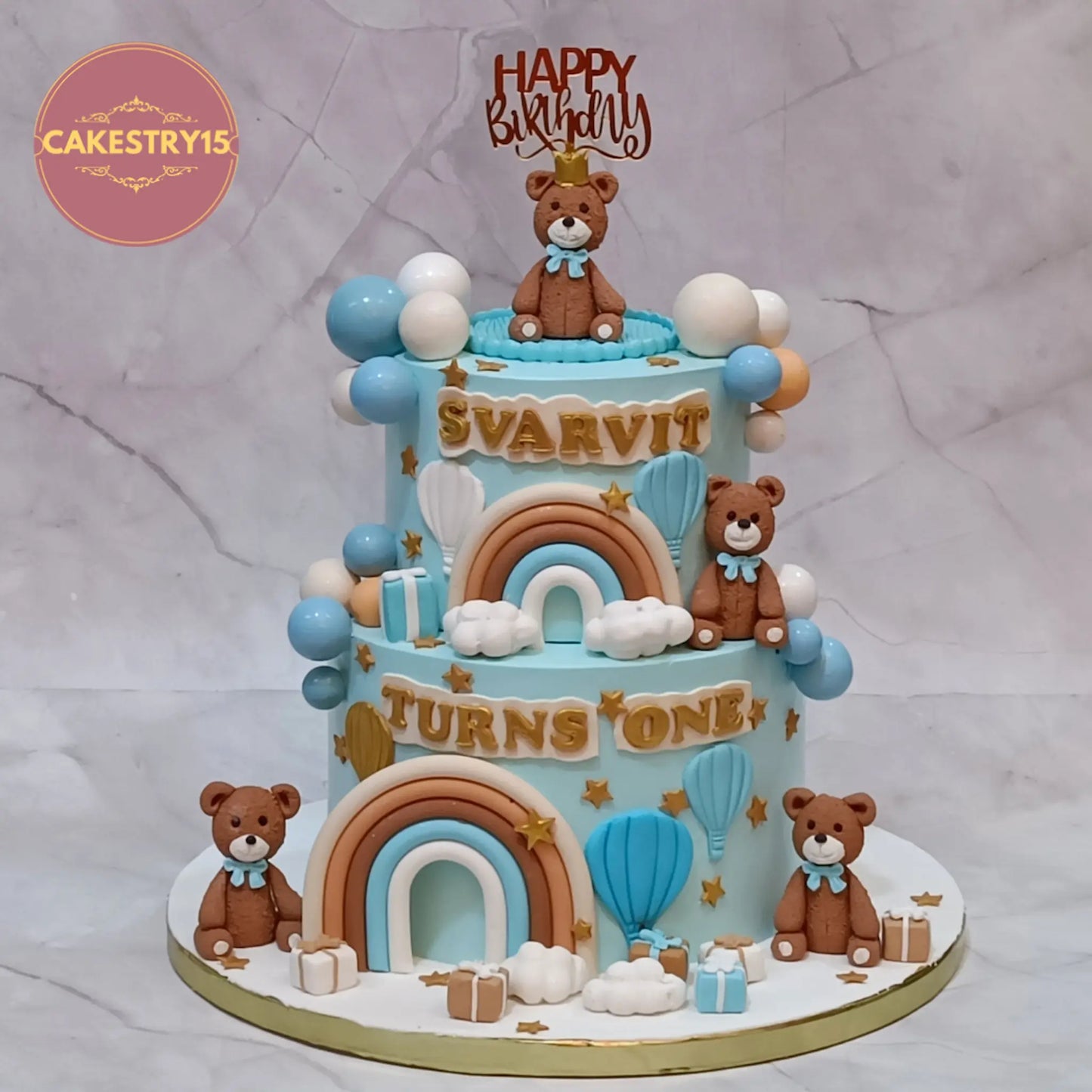 Teddy theme first birthday cake in choco chips with fondant teddies, rainbows, balloons and clouds in Noida