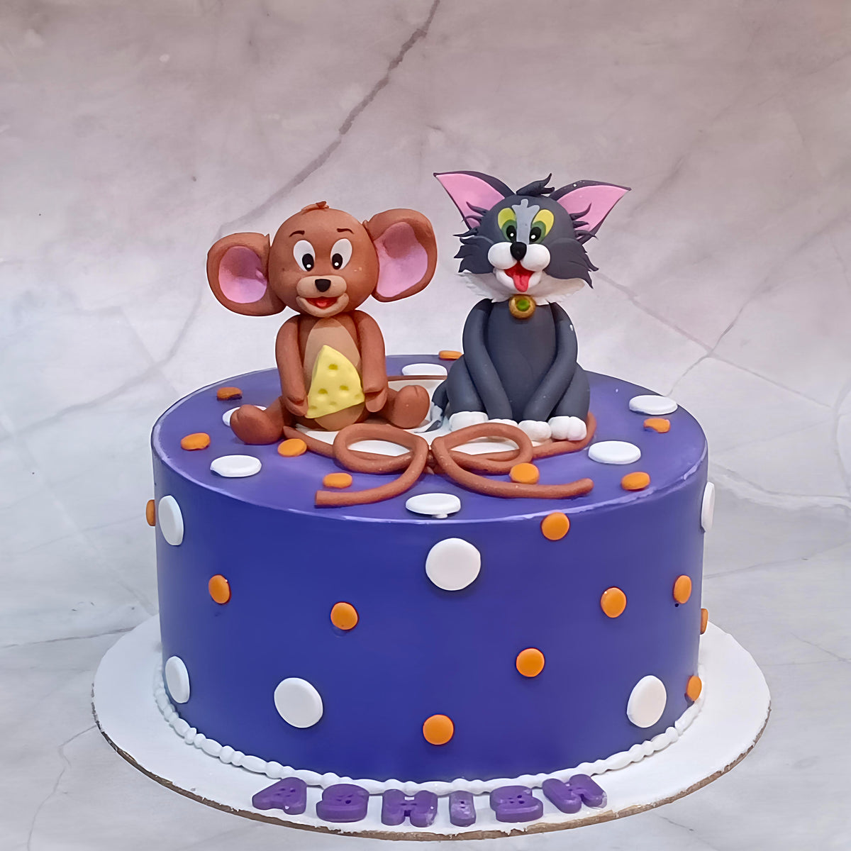 Tom and Jerry theme birthday cake with Tom and Jerry figurines, Jerry holding a cheese block and polka dots all over.