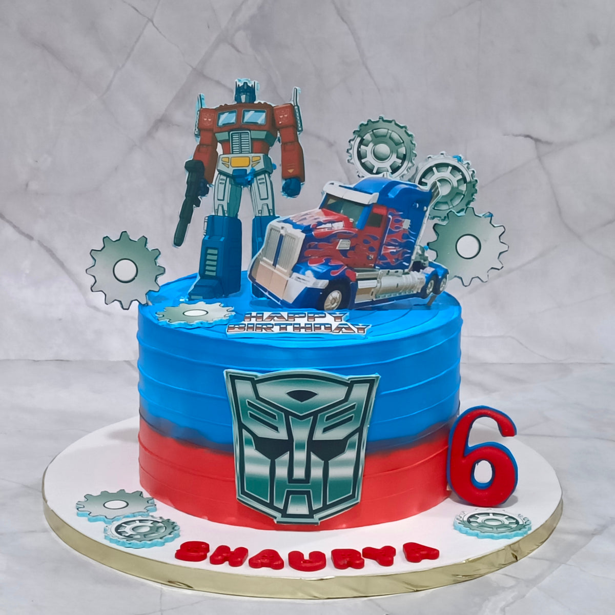 Premium eggless Transformers kids birthday cake with Optimus Prime, blue and red gradient design, and Autobot emblem, a custom theme cake in Noida for a 6th birthday celebration.